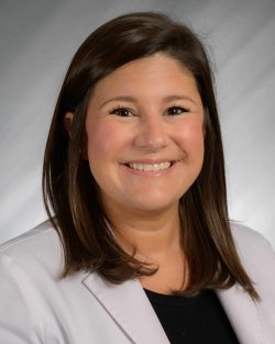A smiling woman in a white jacket with a neutral background.
