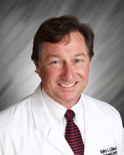 A person in a white coat and striped tie with a gray background.