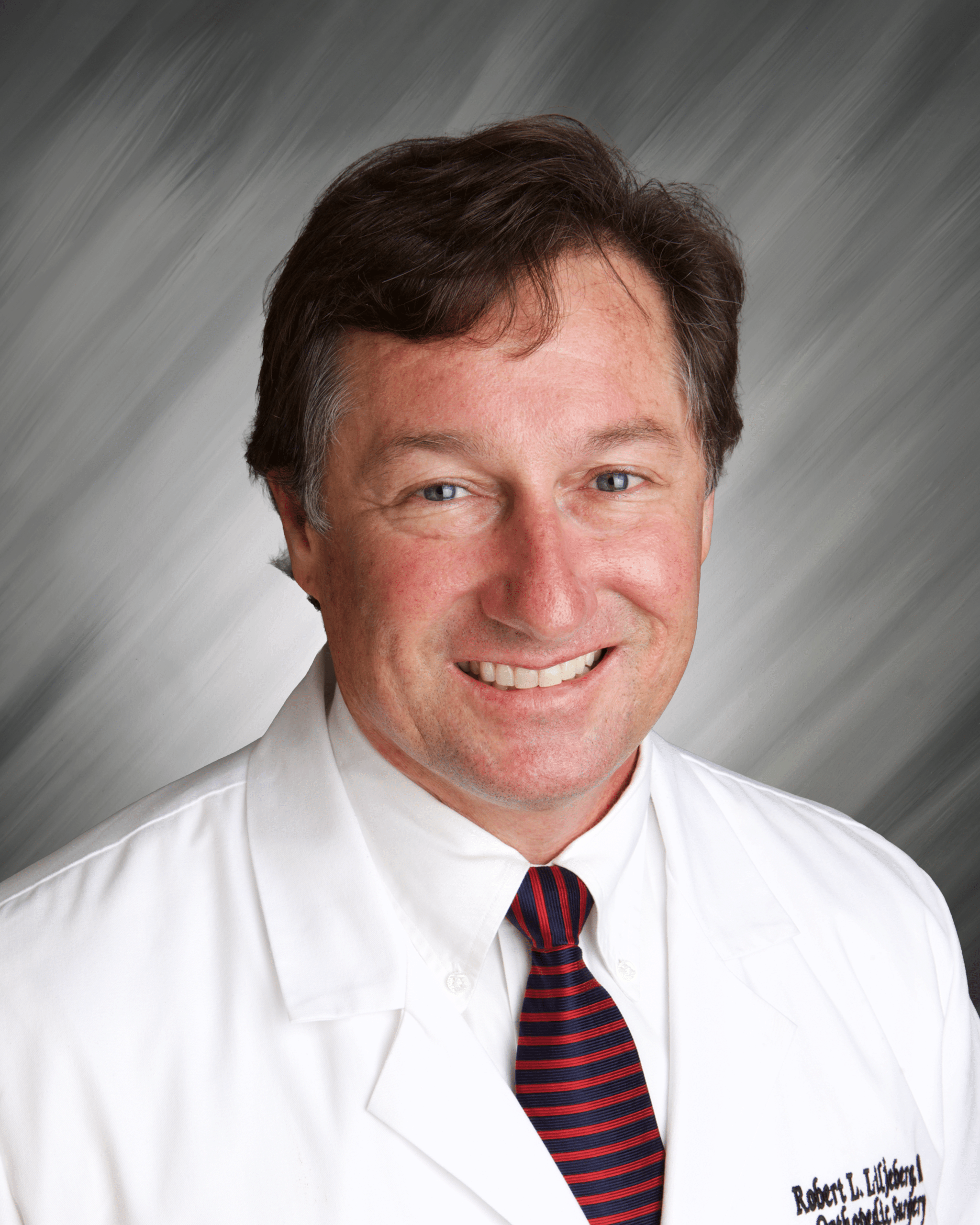 A person in a white coat and striped tie with a gray background.
