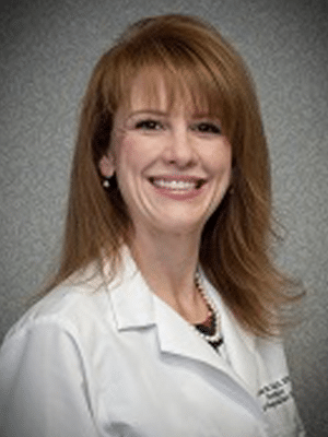 A woman in a white coat smiling against a gray background.