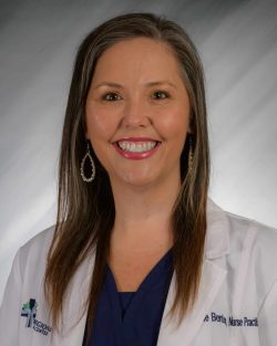 Woman smiling in a professional white coat with a blurred gray background.