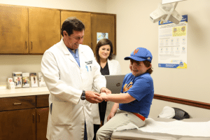 Doctor examining smiling child in a baseball cap in a medical office.