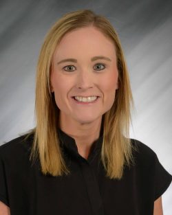 A woman with blonde hair smiling in a black shirt against a gradient background.
