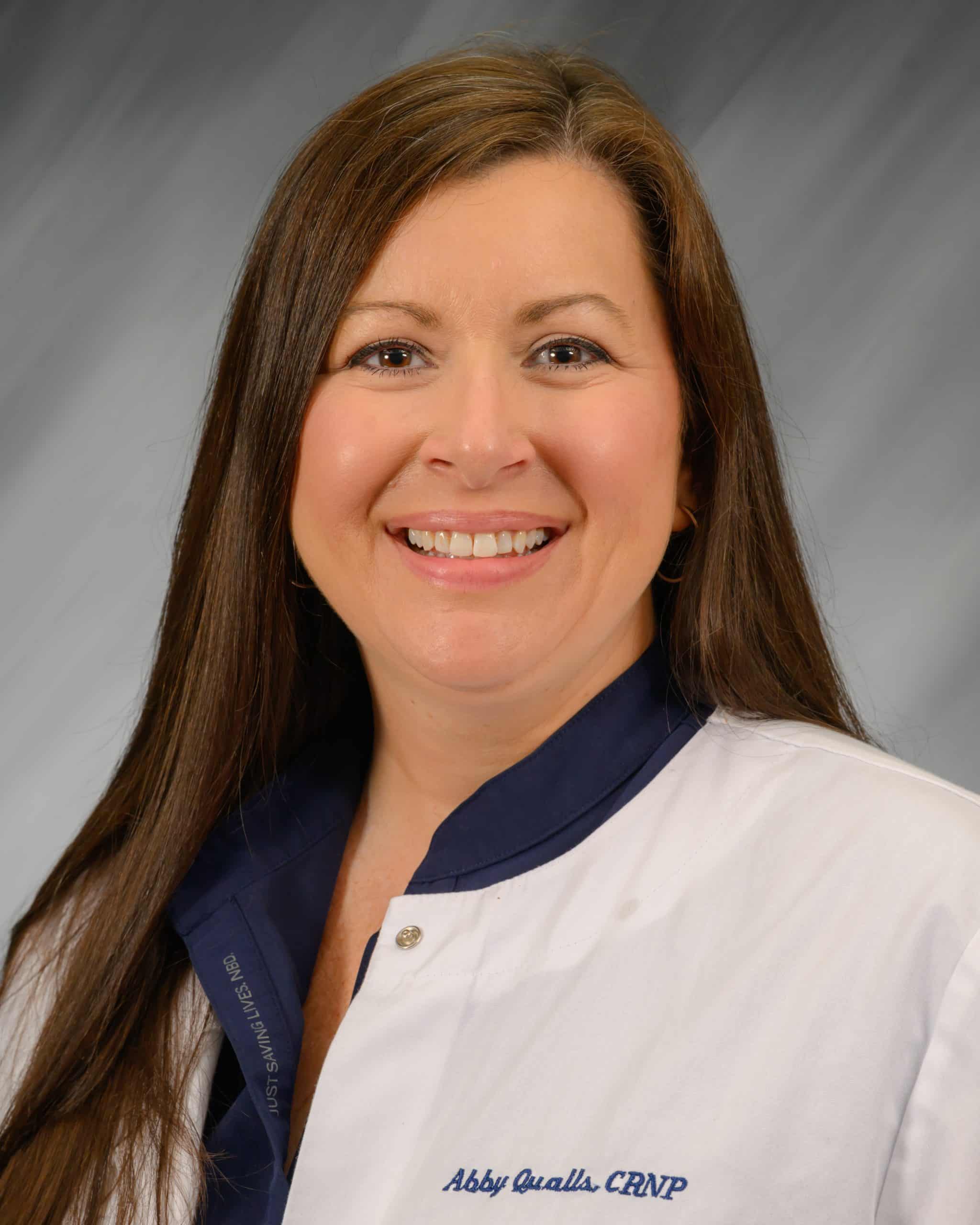 Abby Qualls smiling in a white coat, professional headshot.