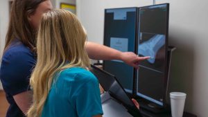 Two medical professionals examining an X-ray on dual monitors.