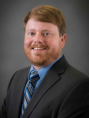 A person in a suit and tie smiling against a gray background.