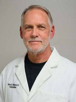 A man in a white lab coat with a neutral expression.