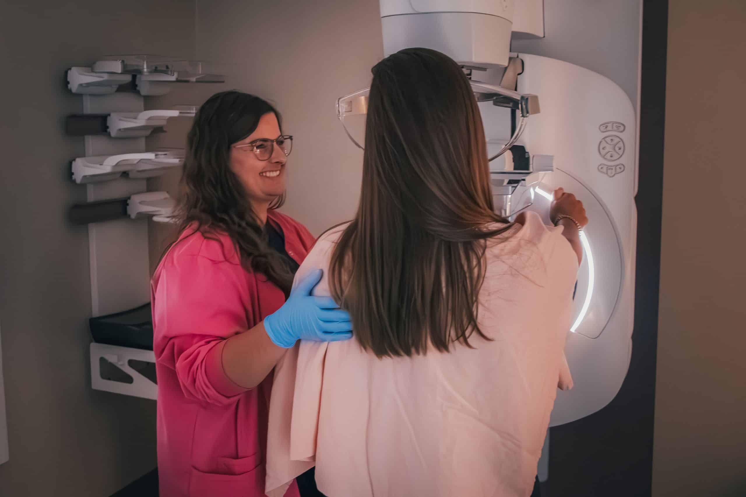 Technician assists a woman during a mammography procedure with medical equipment.