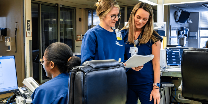 Three healthcare professionals in blue scrubs collaborating in a hospital setting.