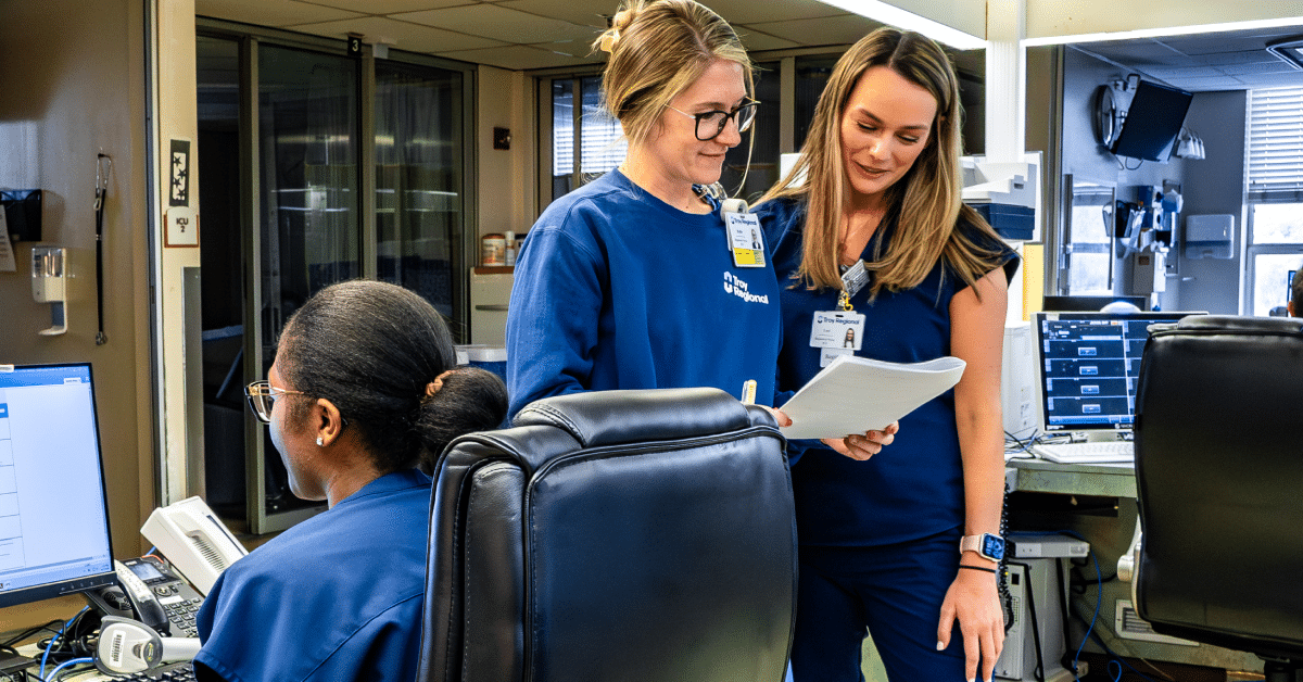 Three healthcare professionals in blue scrubs collaborating in a hospital setting.