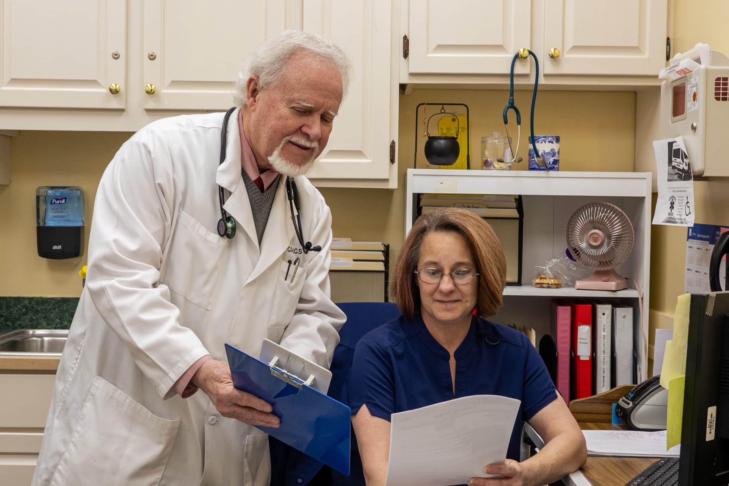 A doctor reviews medical documents with a nurse at a clinic desk.