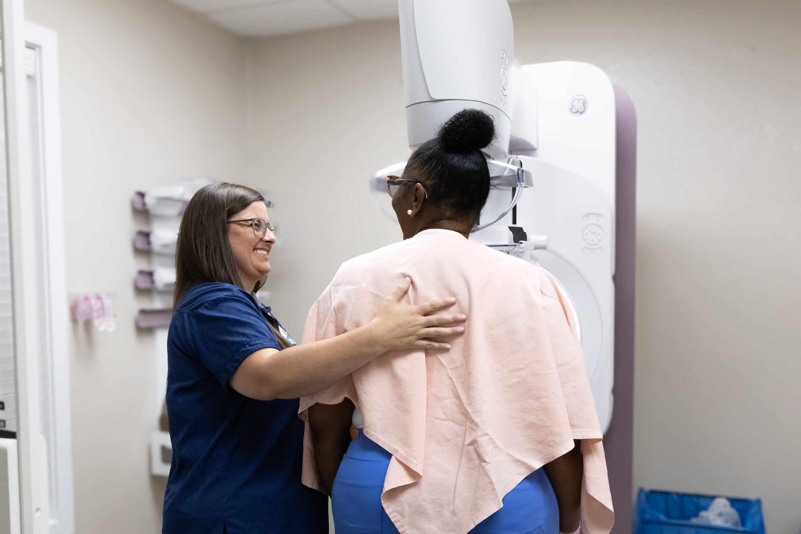 Technician assisting woman during mammogram exam in medical office.