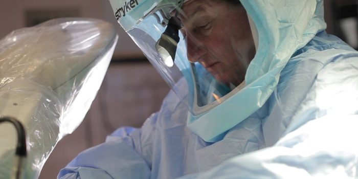 Medical professional in surgical scrubs and protective gear operates in a sterile environment.