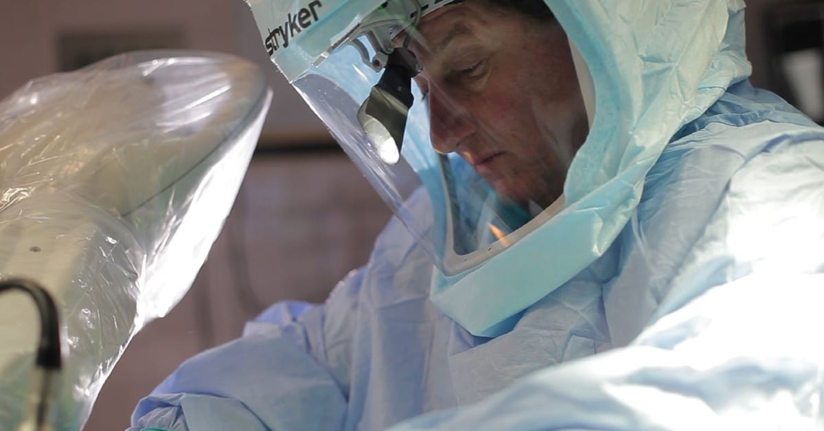 Medical professional in surgical scrubs and protective gear operates in a sterile environment.