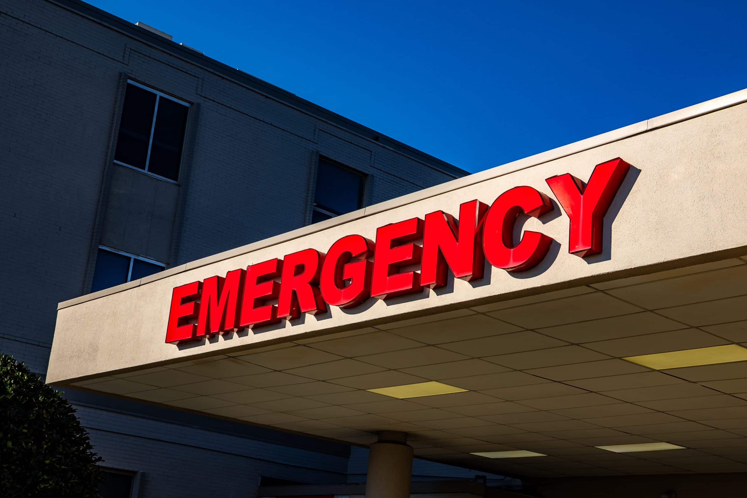 Red EMERGENCY sign on hospital entrance under a clear blue sky.