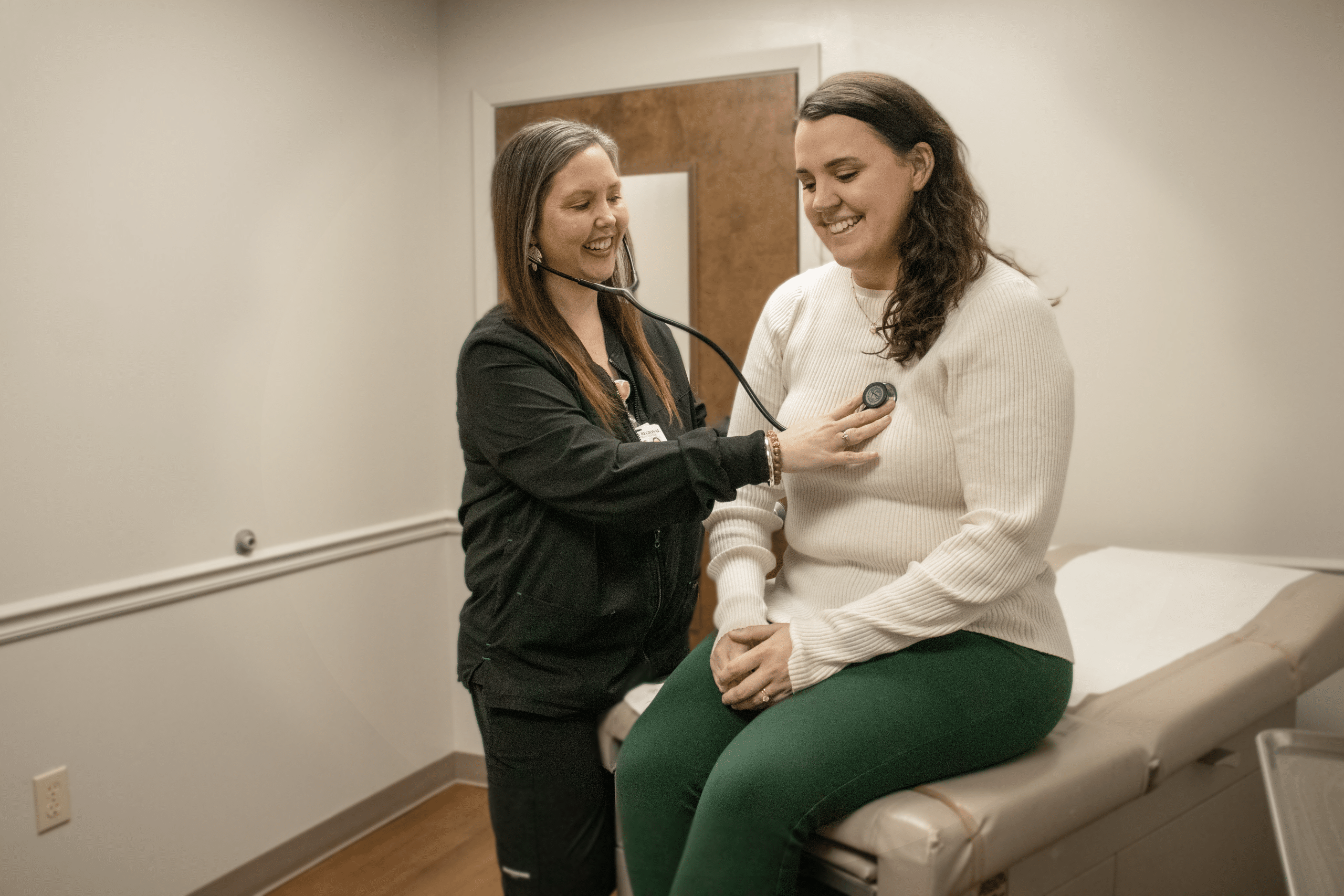 Nurse examines woman with stethoscope in a medical office.