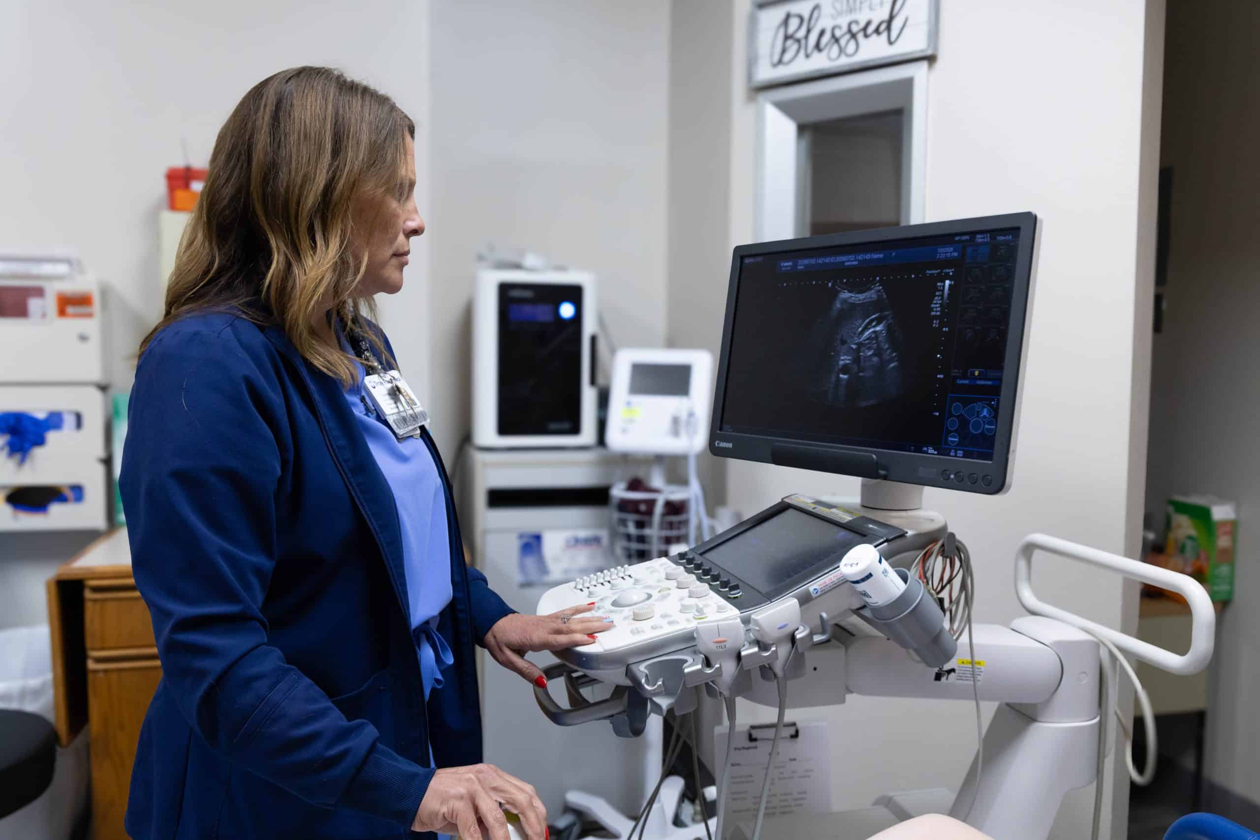 Healthcare worker operating an ultrasound machine in a medical room.