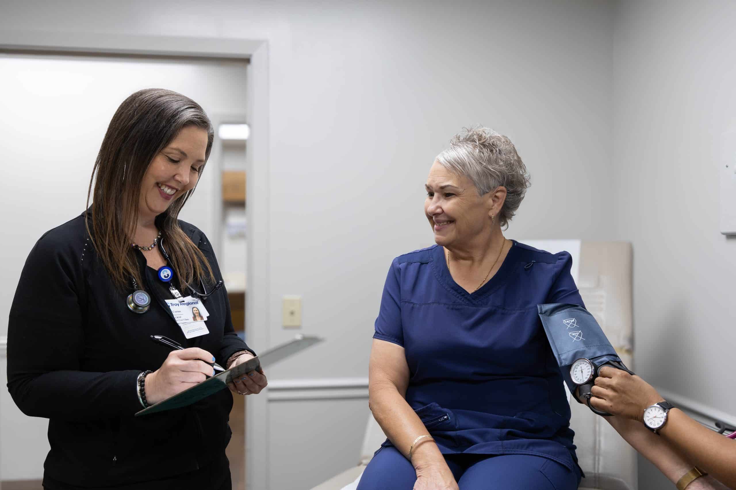Healthcare professional taking a woman's blood pressure while another writes on a clipboard.