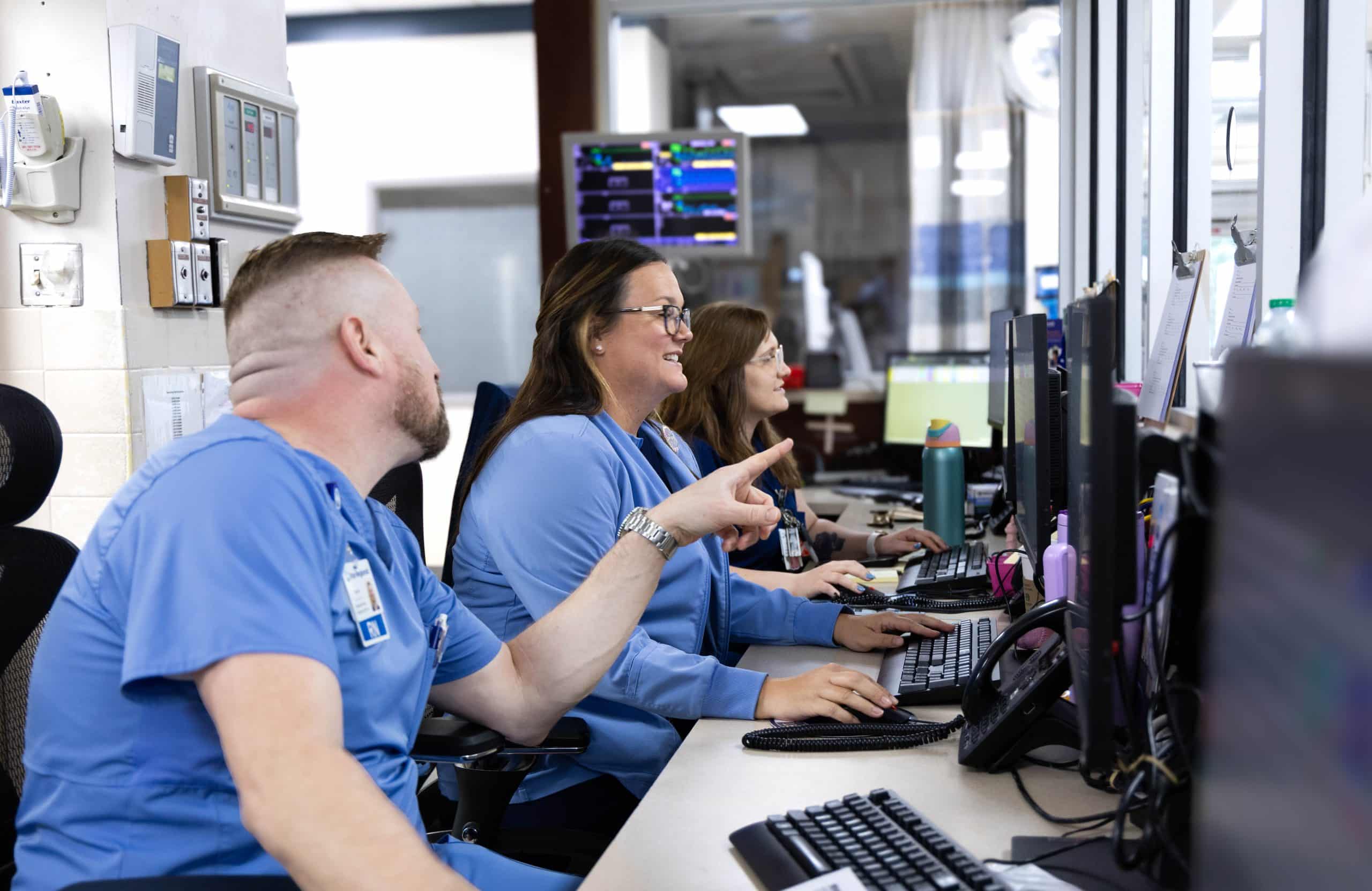 Healthcare workers in blue uniforms collaborating at a computer station.