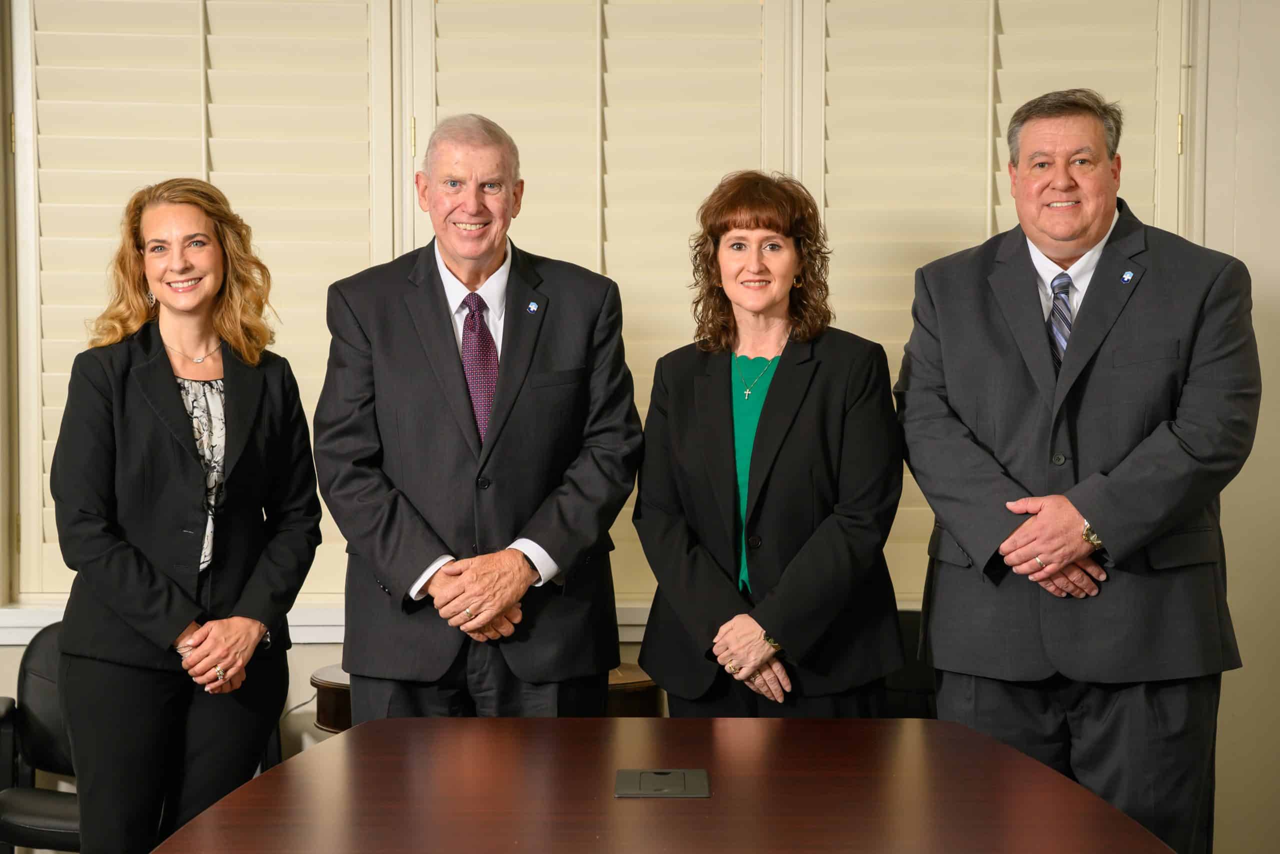 Troy University Four professionals in business attire standing together in an office setting.