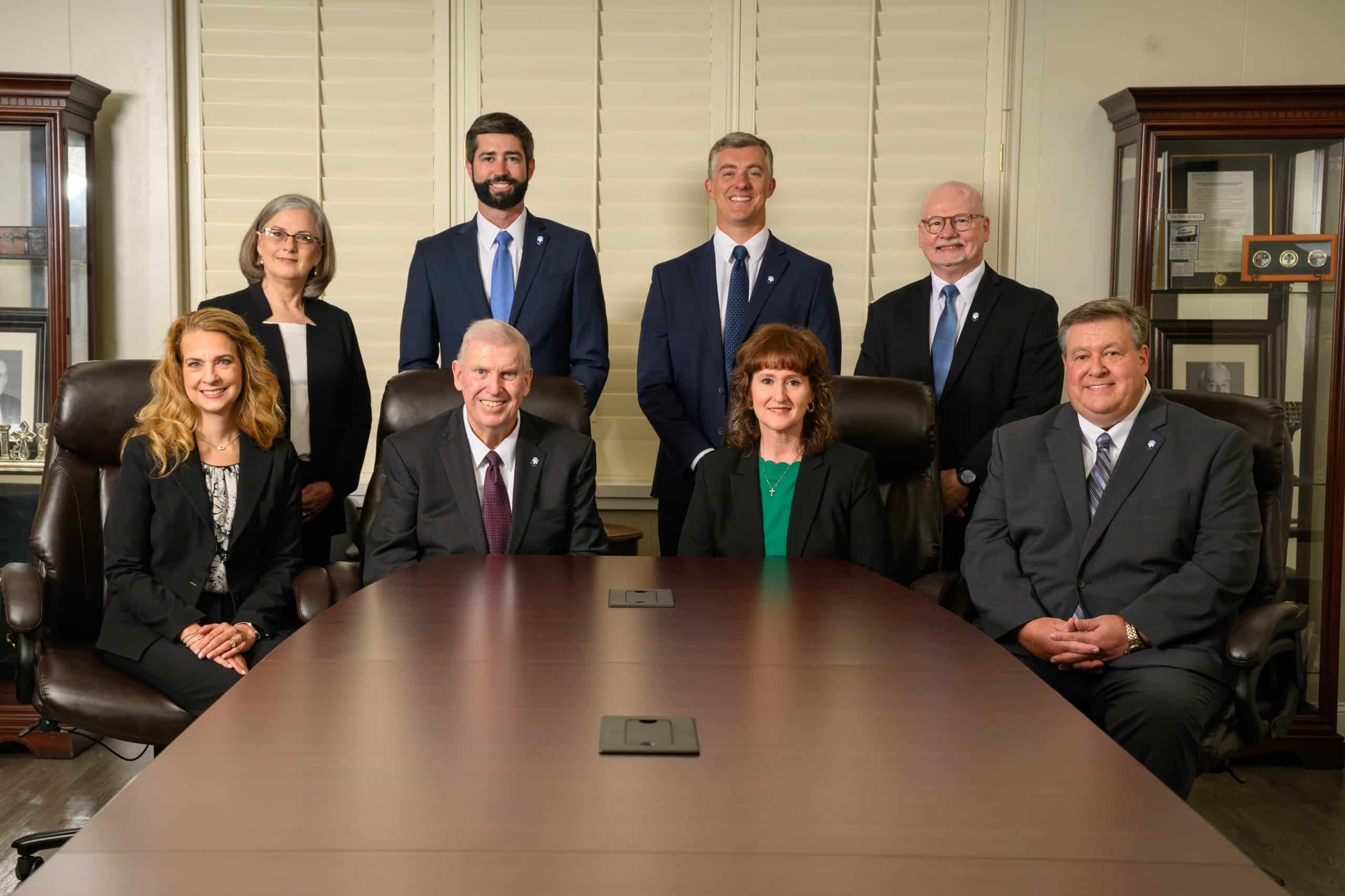 Group of professionals in formal attire around a conference table in an office setting.