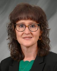 Troy University A woman with glasses and curly hair in a blazer and green top against a gray background.