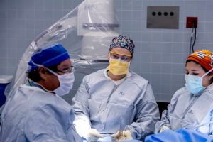 Surgeons in an operating room performing a medical procedure, wearing masks and protective gear.